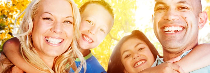 Smiling Happy Family of Four Outside in Forest With Sun Backlighting Them